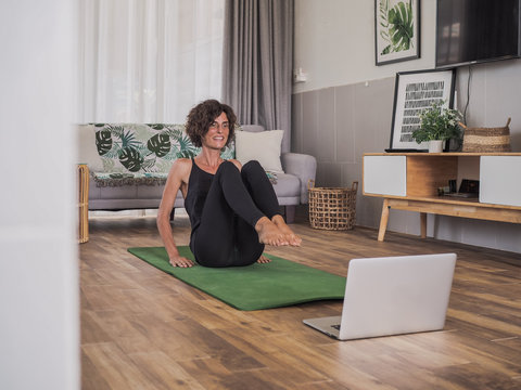 happy and smiling women looking into the laptop in doing a fitness pilates workout in her living room at home