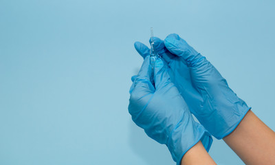 the medic's hands in blue gloves on a blue background open the vial