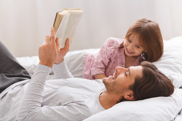 Young father reading book to his little happy daughter