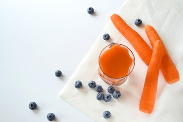 Carrot juice in a glass and blueberries on a white tablecloth