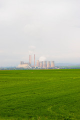 Fototapeta na wymiar Nuclear power plant with green field and big blue clouds