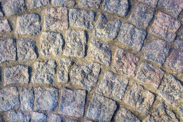 Fragment of the ancient road surface of the shady granite blocks. Horizontal orientation. Selective focus. View from above.