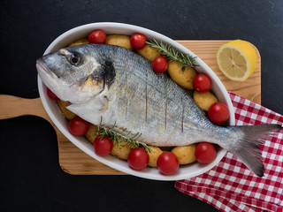 sea bream, tomatos, potatos and rosemary on a serving dish on slate background. ready to cook