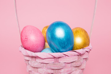 Multi-colored Easter eggs in a basket on a pink isolated background. Easter is a bright holiday.