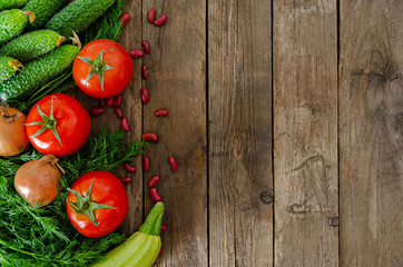 Fresh rustic vegetables on an old wooden table - tomatoes, cucumbers, onions, dill, beans.