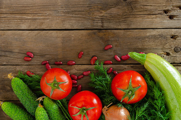 Fresh rustic vegetables on an old wooden table - tomatoes, cucumbers, onions, dill, beans.
