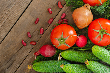 Fresh rustic vegetables on an old wooden table - tomatoes, cucumbers, onions, dill, beans, radishes.