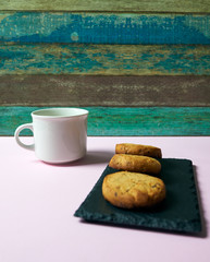 
Homemade butter cookies and a white cup on a pink table and wooden background. The image has space for a text.
