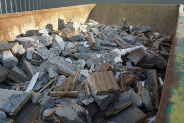 Building waste and debris from a demolished building, pieces of mortar, wood, polystyrene and concrete mostly in grey color in a bit waste container