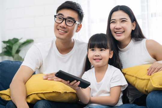 Happy Asian family spending time by watching tv together on sofa in living room. family and home concept