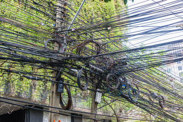 Messy and untidy electrical cables hanging from an electricity pole in Thailand