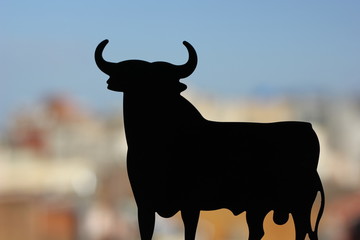 Figurine of a black bull with horns on a colorful background of the city