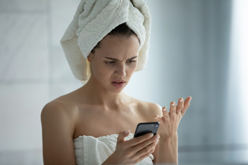 Frustrated young woman after shower stand in bathroom having problems using smartphone gadget,...