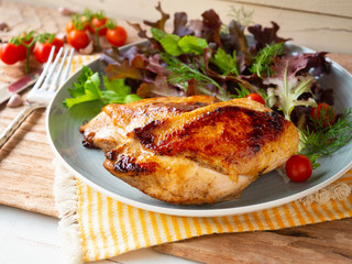 Grilled chicken breast steak serves with fresh cherry tomato and salad on a grey color dish.