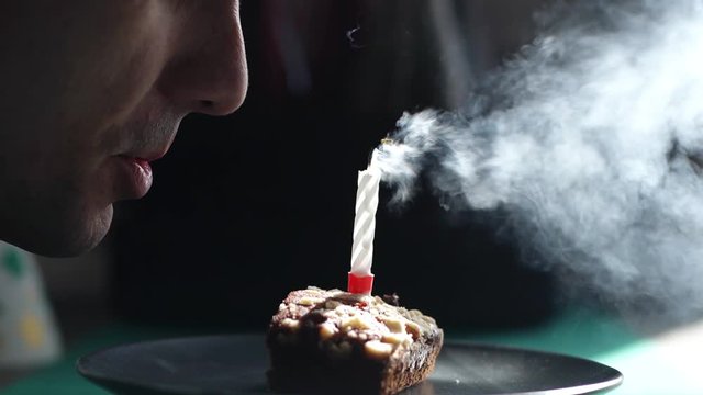 Close-up of face of man blowing out one candle on little cake. Smoke hovers beautifully in the air. Shooting in slow motion.
