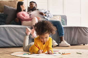 Couple on couch and daughter drawing on floor