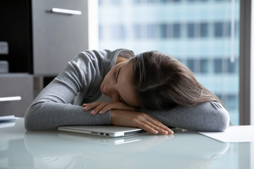 Exhausted young woman worker lying on desk in office fall asleep on laptop, tired millennial female employee take nap daydream at workplace, feel fatigue or exhaustion, overwork concept