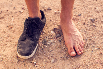 Men's feet with one dirty shoe outdoor. Poverty concept