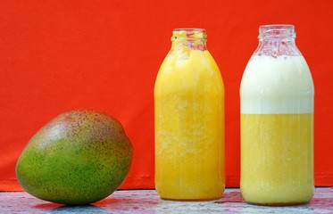 Glass bottles filled with colorful fresh homemade mango smoothies on an orange background