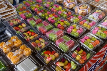 Plastic containers containing Luk Chub, a traditional Thai multi-coloured sweet dessert made from ground mung beans, coloured and hand shaped, at a market stall, Thailand