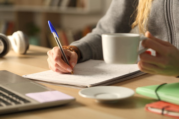 Student hands holding coffee cup writing at night
