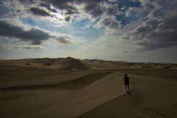 Fototapeta na wymiar Person walking on sand dune and looking into the distance in the desert of Huacachina, Ica, Peru