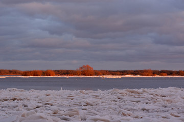 Spring landscape of the river during the ice drift. Ice floes on the background of the river and the shore with trees lit by the sun. Volkhov River © Aleksandr Kalegin