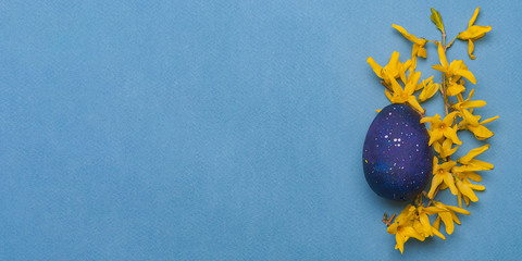 Blue easter egg with yellow flowers on a blue background. Top view.