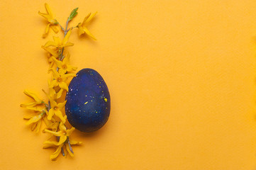 Blue easter egg with yellow flowers on a yellow background. Top view.