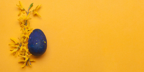 Blue easter egg with yellow flowers on a yellow background. Top view.