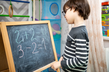Studying at home. The kid learns to count numbers on the board. Portrait of a cute happy school child boy at home doing homework. Primary school and education.