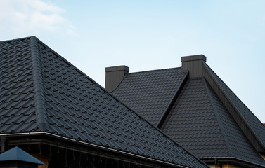 Fototapeta na wymiar Black metal tile roof. Roof metal sheets. Modern types of roofing materials. Roof of the house, metal roof tile against the blue sky. Building.