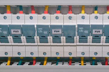 A series of three-phase fuse holders or cylindrical fuse breakers in an electrical Cabinet. Color-coded cables or wires are connected to the breakers.
