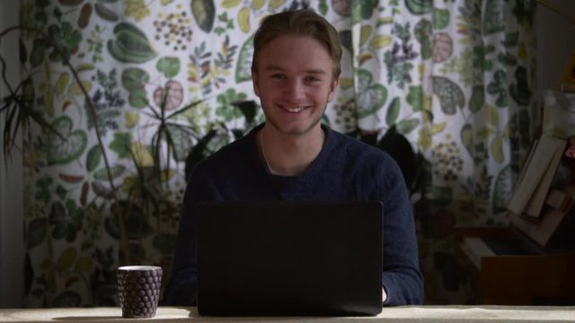 Young white student male sitting at home studying/Working from his laptop -  The smile represent the enjoyment of distant working.
Concept: Studying/working from home office, Man smile, Business