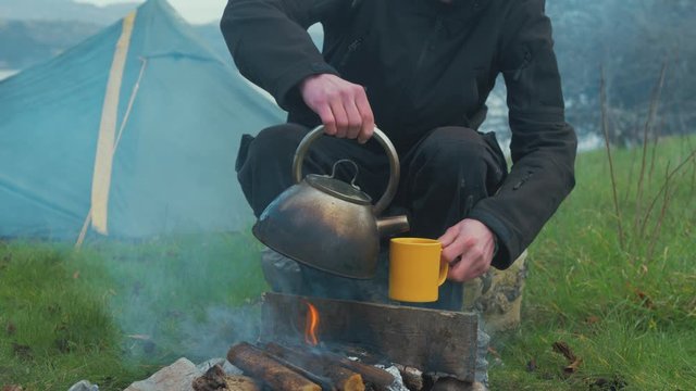 Man making cup of coffee solo camping by fire 4K