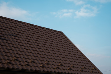 Fototapeta na wymiar Brown metal tile roof. Roof metal sheets. Modern types of roofing materials. Roof of the house, metal roof tile against the blue sky. Building.