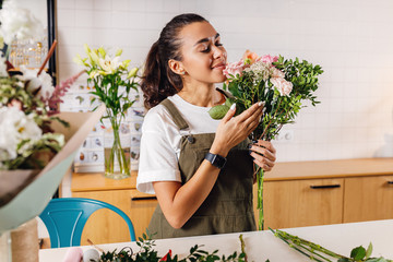 Beautiful florist woman holds a bouquet and smelling flowers with closed eyes