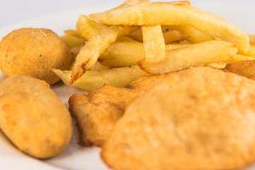 Plate of breaded chicken breast with croquettes and French fries.
