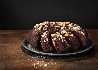 Delicious Homemade Chocolate Bundt Cake with melted chocolate and Sliced Almonds on dark background, copy space. Close up view, horizontal composition, selective focus.