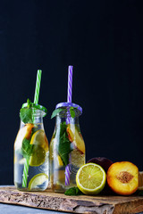 Refreshing fruit drinks with lemon, mint, peach in glass bottles and tubes on the table.