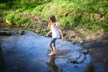 Child cute blond girl playing in the creek. Girl walking barefoot in forest stream  and exploring nature. Summer children fun. Children summer activities
