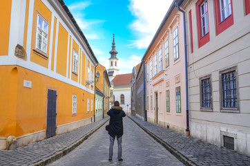 Old town street and buildings with colorful facades in the historical center of Budapest, Hungary. Lutheran Church of Budavar in the background. Traveller taking photo in the middle of the street