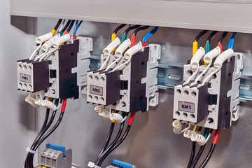 Three contactors or magnetic starters with front additional contacts are arranged in a row in the electrical Cabinet. Wires and cables are connected to the starters and additional contacts.