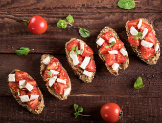 Bruschetta with tomatoes, mozzarella cheese and basil on wooden background. Top view
