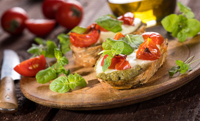 Bruschetta with tomatoes, mozzarella cheese, pesto and fresh basil on wooden background.