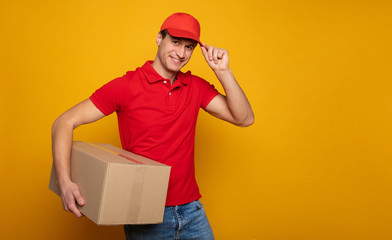 Handsome young happy courier or delivery man in red uniform is posing isolated on yellow background.