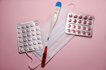 Аmpoule, tablets, thermometer and mask  against coronavirus on a pink background.