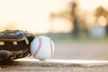 Baseball glove and ball on park sport field at sunset close up, copy space on blurred background.