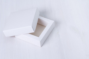 Open empty white gift box with a lid on isolated wooden background. Side view, square box. Elegant eco-friendly mockup. Isolated cardboard box with cover on white table. Empty space on the right