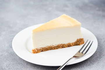 Slice of plain cheesecake on white plate. Dessert cake made with cream cheese. Isolated on grey concrete background